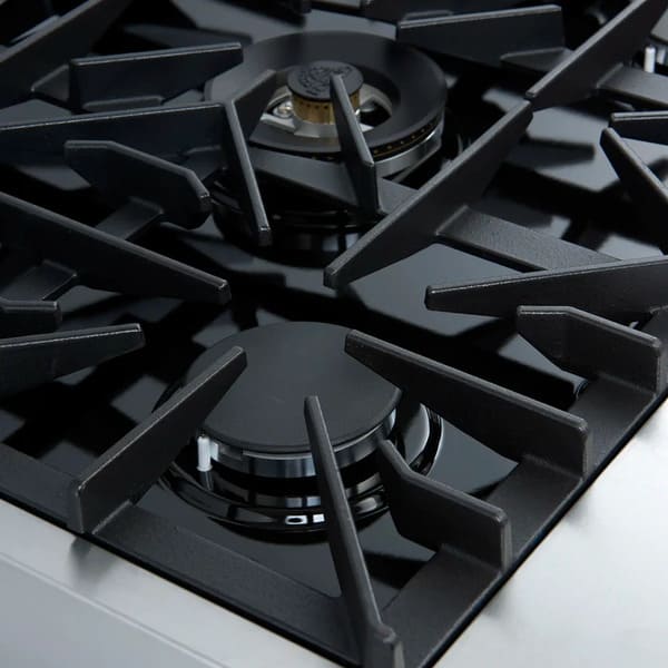 Close-up angled view of a brass burner on the FORNO Giovanni 30-Inch Gas Range in black, highlighting precision flame ports, heavy-duty cast iron grate, and matte black cooktop surface.